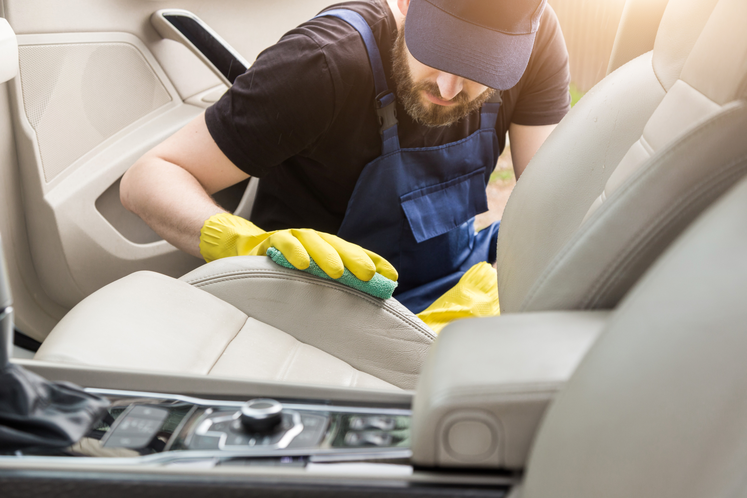 Cleaning service. Man in uniform and yellow gloves washes a car interior in a car wash. Worker washes the chairs of the leather salon